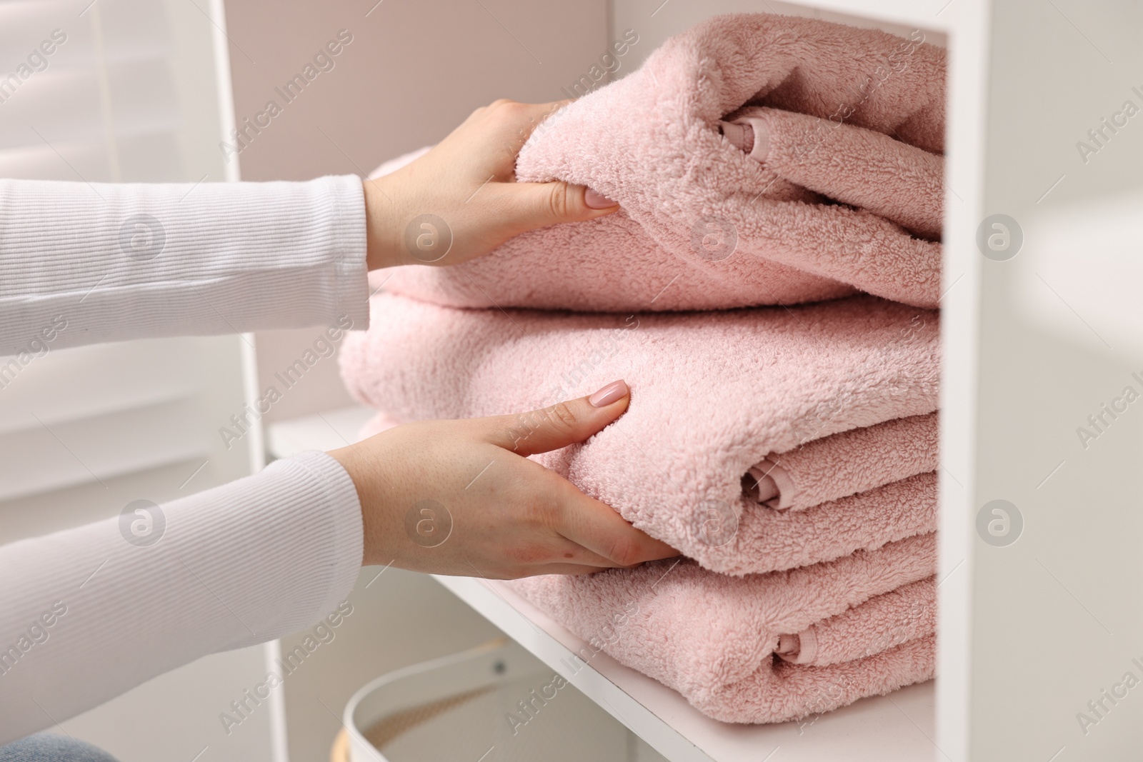 Photo of Woman stacking clean towels on shelf indoors, closeup