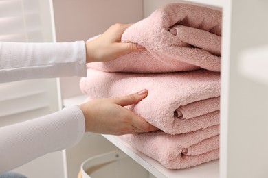 Woman stacking clean towels on shelf indoors, closeup