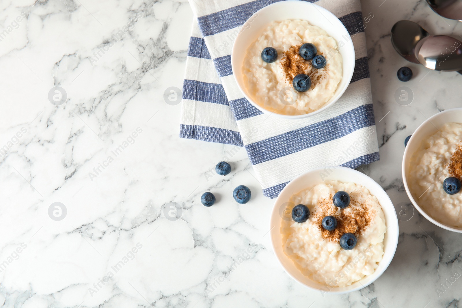 Photo of Creamy rice pudding with cinnamon and blueberries in bowls served on marble table, top view. Space for text