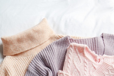 Photo of Stylish knitted sweaters on white fabric, flat lay