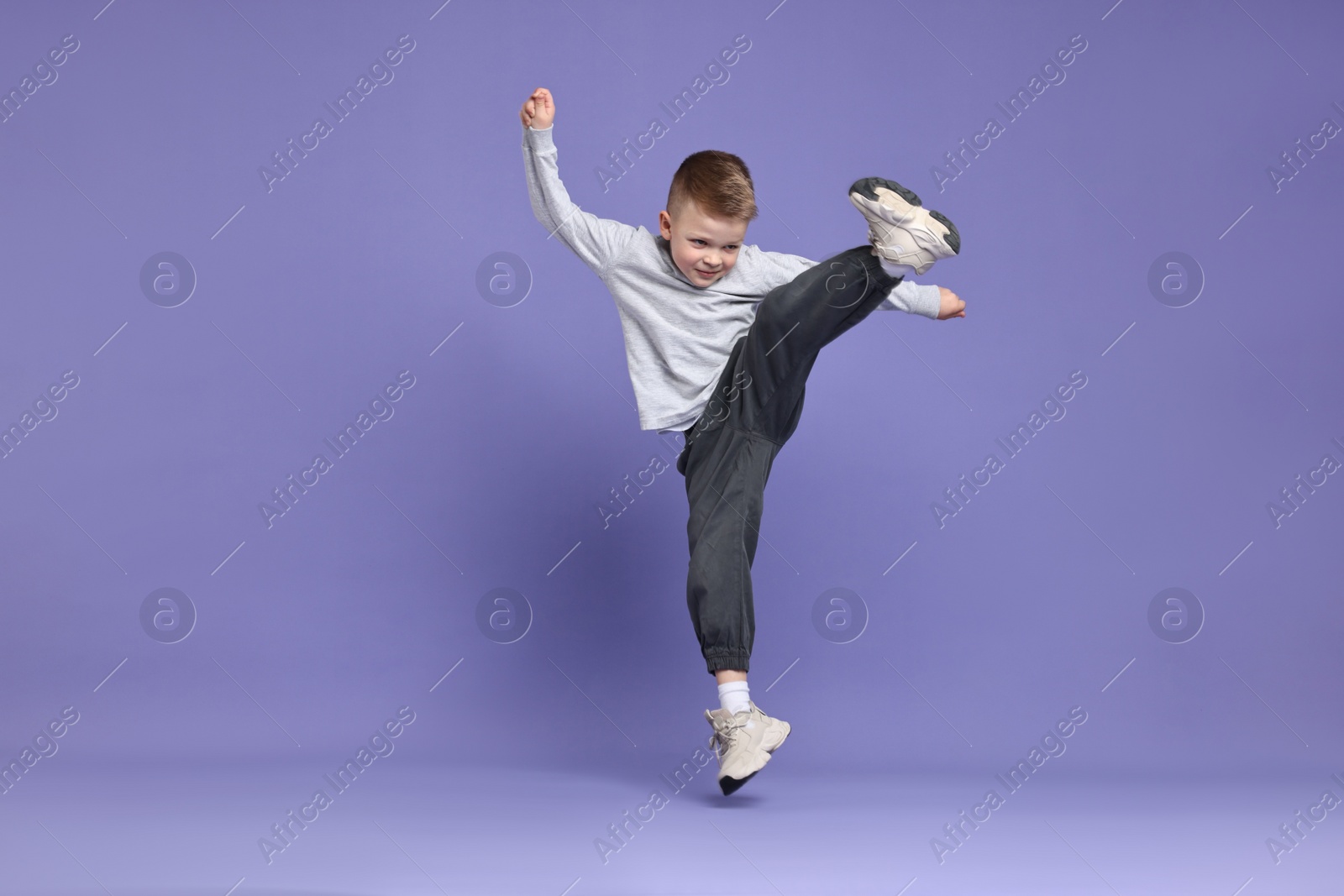 Photo of Happy little boy dancing on violet background. Space for text