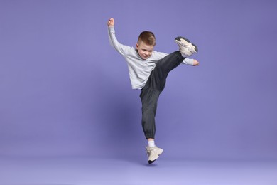 Happy little boy dancing on violet background. Space for text