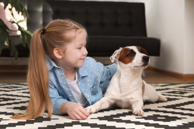 Photo of Cute little girl with her dog on carpet at home. Childhood pet