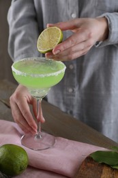 Photo of Woman squeezing lime juice into glass with delicious Margarita cocktail at wooden table, closeup