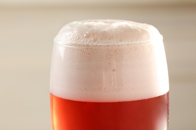 Photo of Glass of red tasty beer with foam, closeup