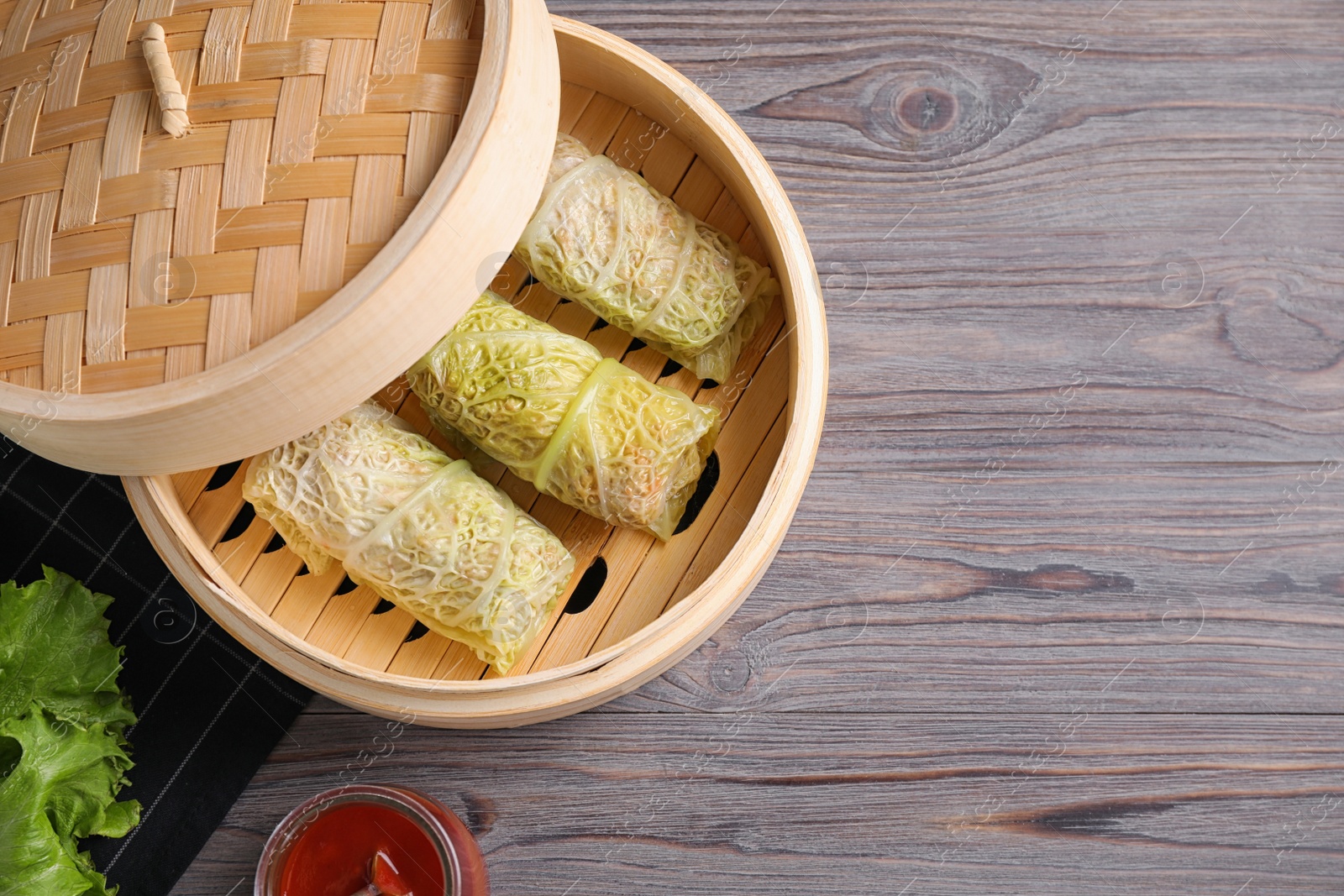 Photo of Delicious cabbage rolls in bamboo steamer on wooden table, flat lay. Space for text