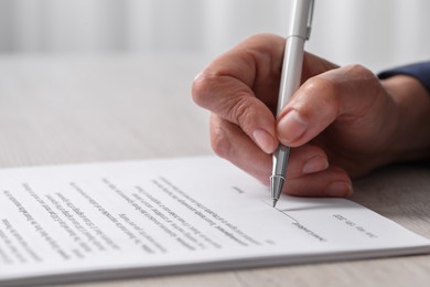 Photo of Woman signing document at light wooden table indoors, closeup. Space for text