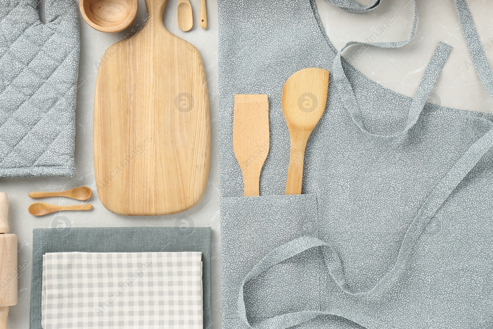 Photo of Kitchen napkins, apron and different utensils on light grey table, flat lay