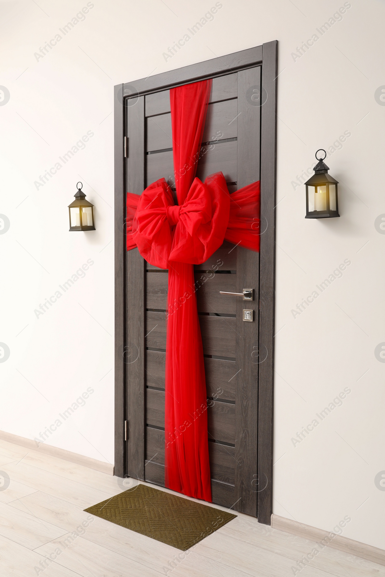 Photo of Wooden door with beautiful red bow and lanterns hanging on wall. Christmas decoration