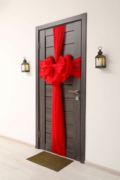 Wooden door with beautiful red bow and lanterns hanging on wall. Christmas decoration