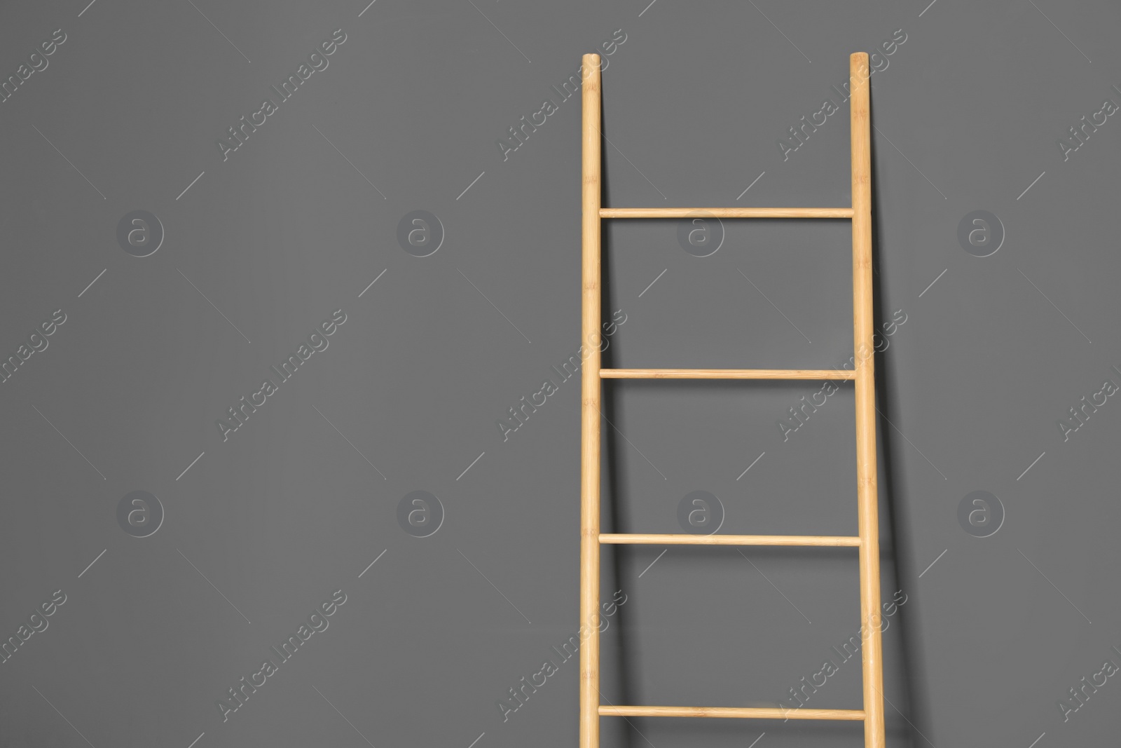 Photo of Modern wooden ladder on grey background. Space for text