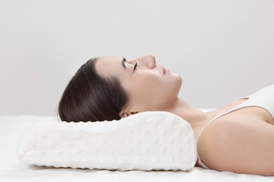 Photo of Woman sleeping on orthopedic pillow against light grey background