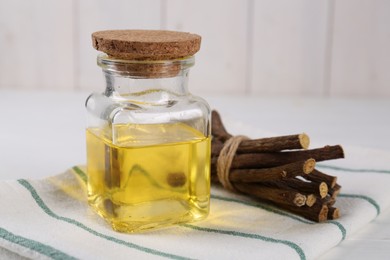 Photo of Dried sticks of licorice roots and essential oil on white table, closeup