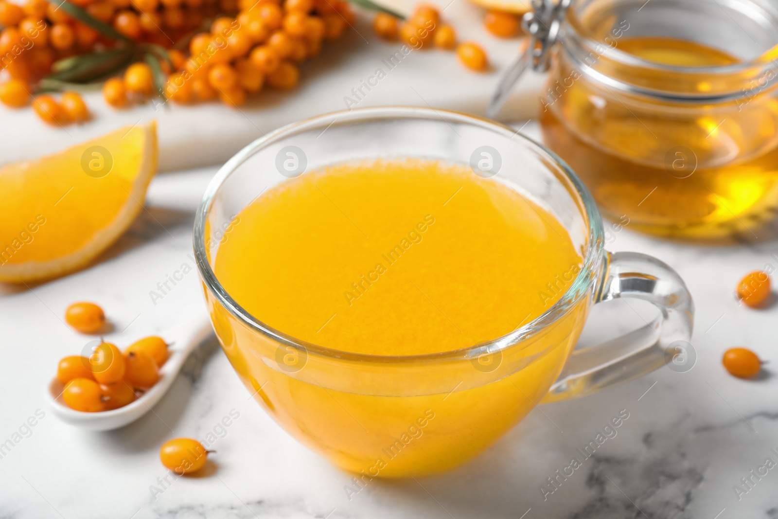 Photo of Fresh sea buckthorn tea on white marble table, closeup