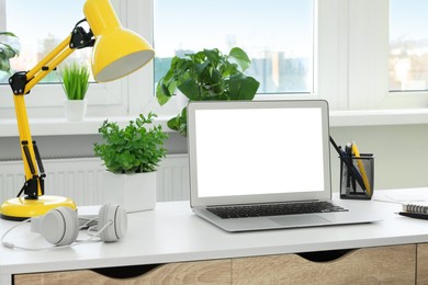 Image of Comfortable workplace at home. Modern laptop with blank screen and lamp on white desk. Mockup for design