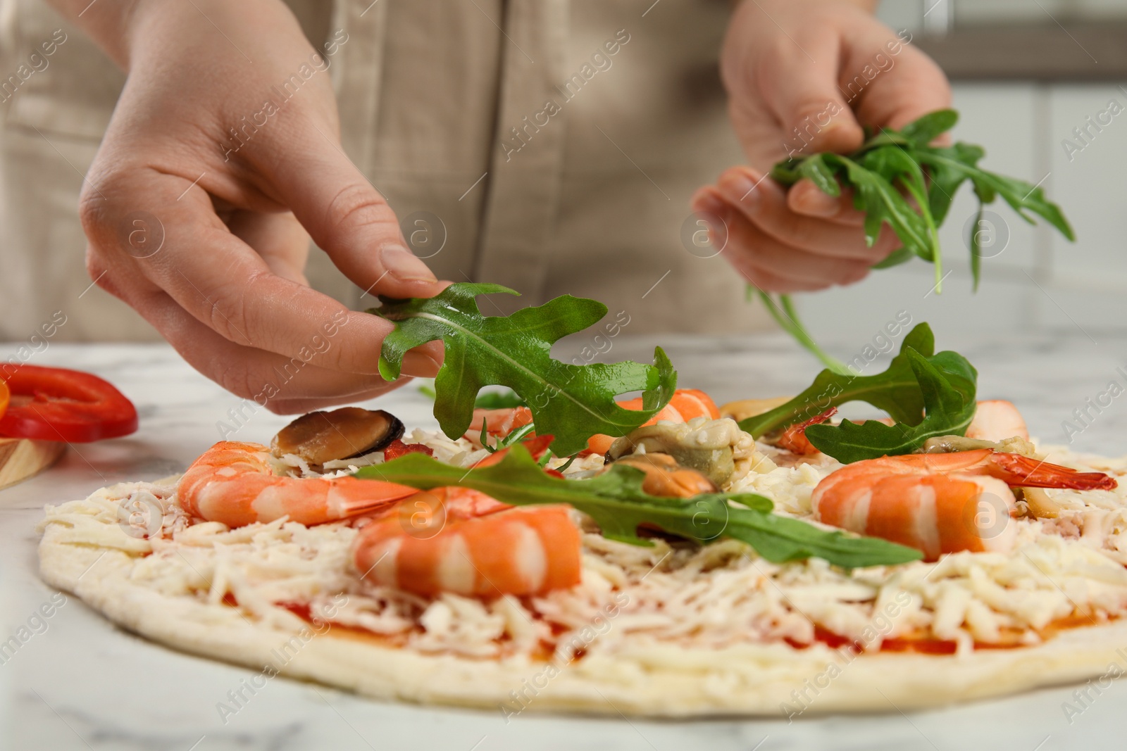 Photo of Woman adding arugula to pizza white marble table, closeup