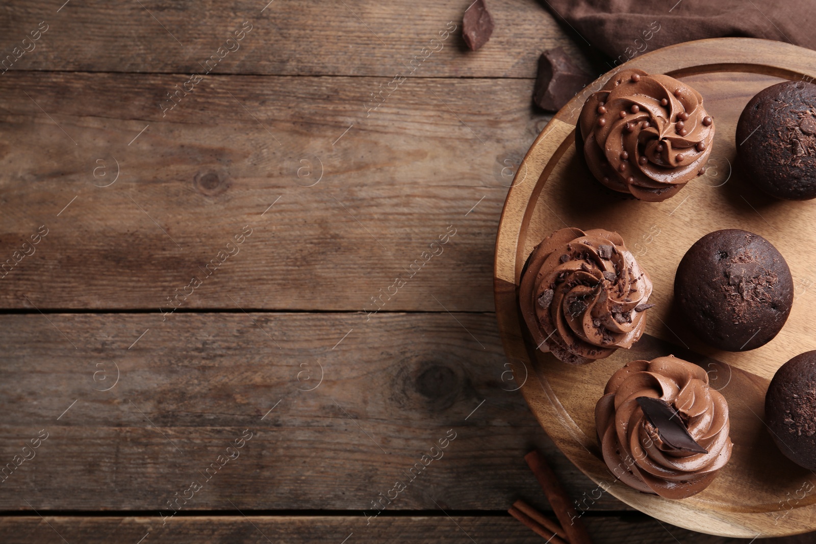 Photo of Delicious chocolate muffins and cupcakes decorated with cream on wooden table, top view. Space for text