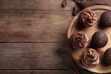 Photo of Delicious chocolate muffins and cupcakes decorated with cream on wooden table, top view. Space for text