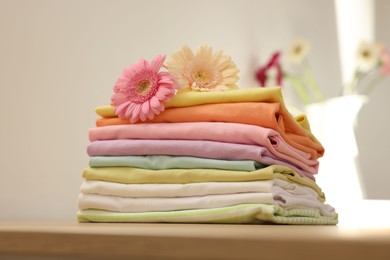 Photo of Stack of clean clothes and flowers on table