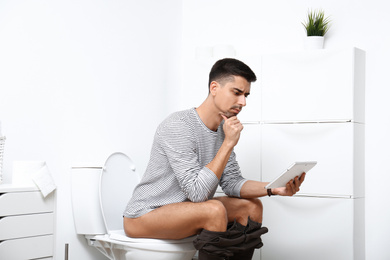 Photo of Man with tablet sitting on toilet bowl in bathroom