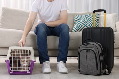 Photo of Travel with pet. Man near carrier with cute cat on sofa at home, closeup