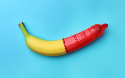 Photo of Banana with condom on light blue background, top view. Safe sex concept