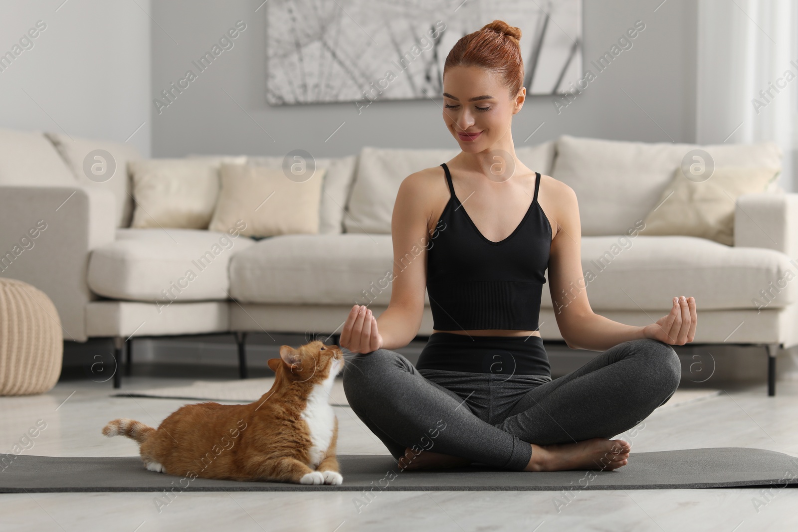 Photo of Beautiful woman with cute red cat practicing yoga on mat at home