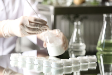 Photo of Scientist working in cosmetic laboratory, focus on jars with cream