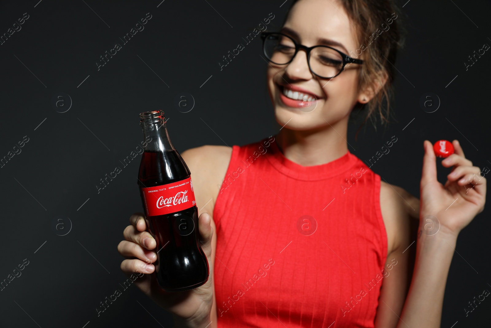 Photo of MYKOLAIV, UKRAINE - NOVEMBER 28, 2018: Young woman with bottle of Coca-Cola and cap on dark background