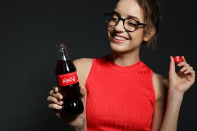 MYKOLAIV, UKRAINE - NOVEMBER 28, 2018: Young woman with bottle of Coca-Cola and cap on dark background