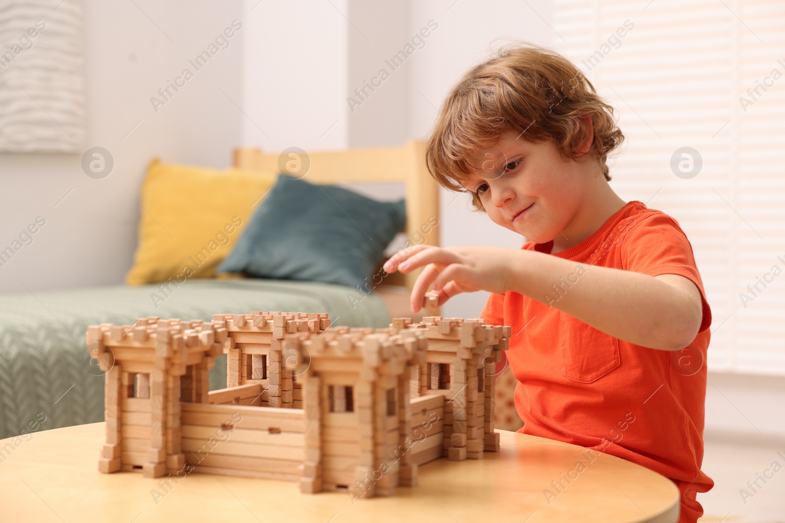 Photo of Cute little boy playing with wooden fortress at table in room. Child's toy