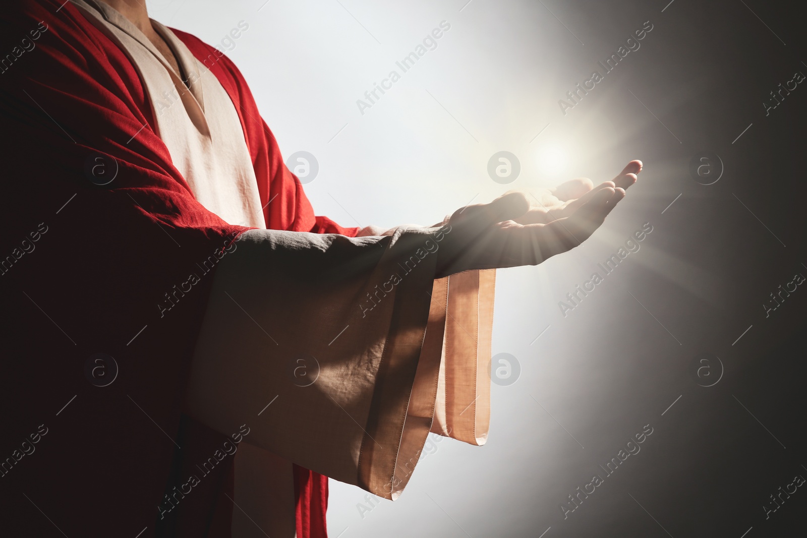 Image of Jesus Christ on grey background, closeup. Miraculous light in hands