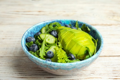 Photo of Delicious avocado salad with blueberries in bowl on white wooden table