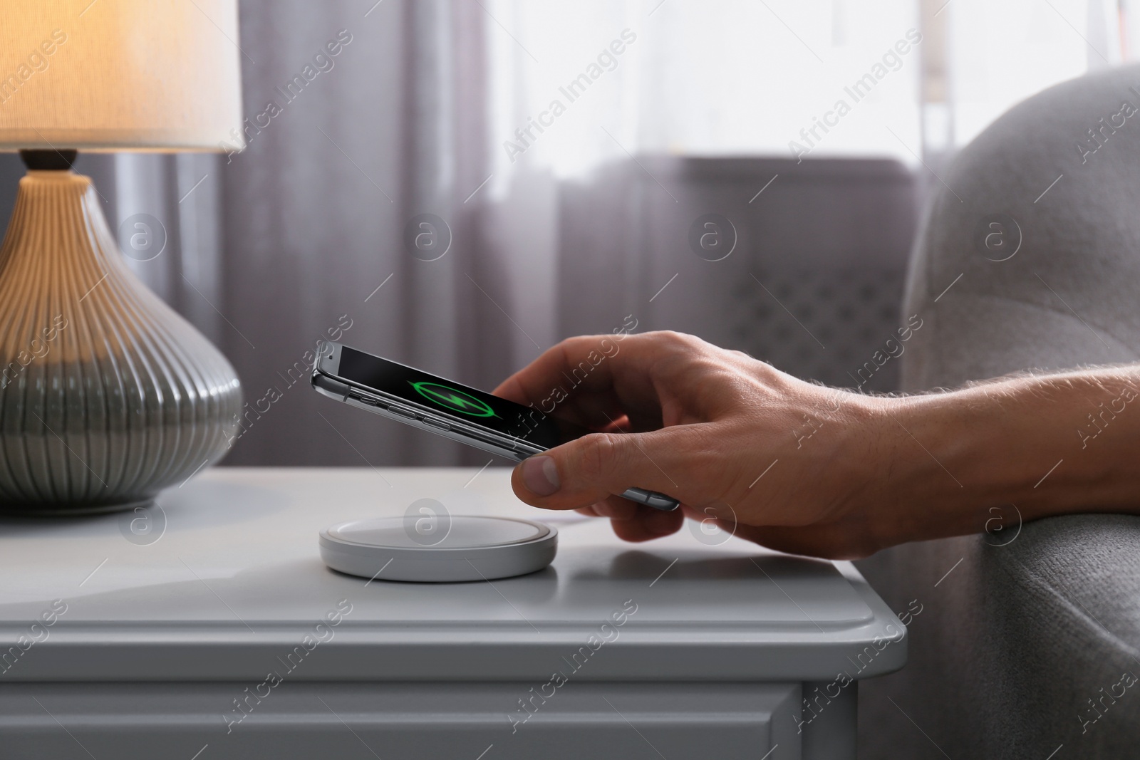 Photo of Man putting smartphone on wireless charger in room, closeup