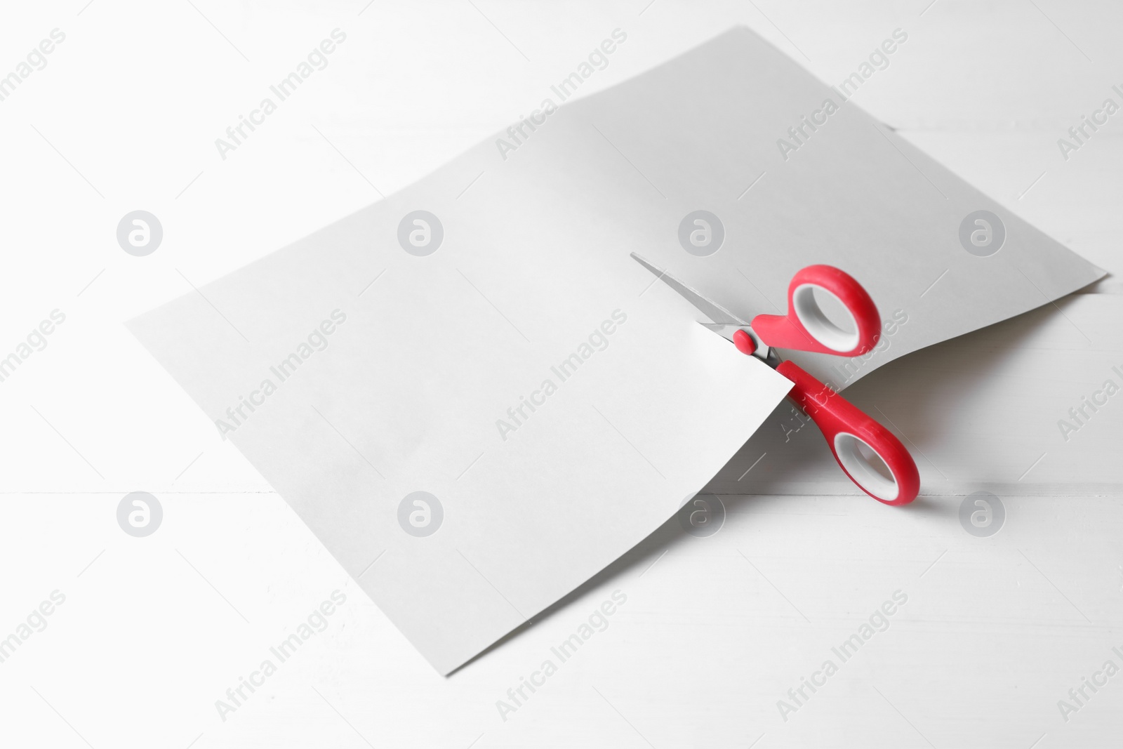 Photo of Red scissors cutting paper on white wooden background