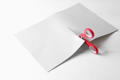 Photo of Red scissors cutting paper on white wooden background