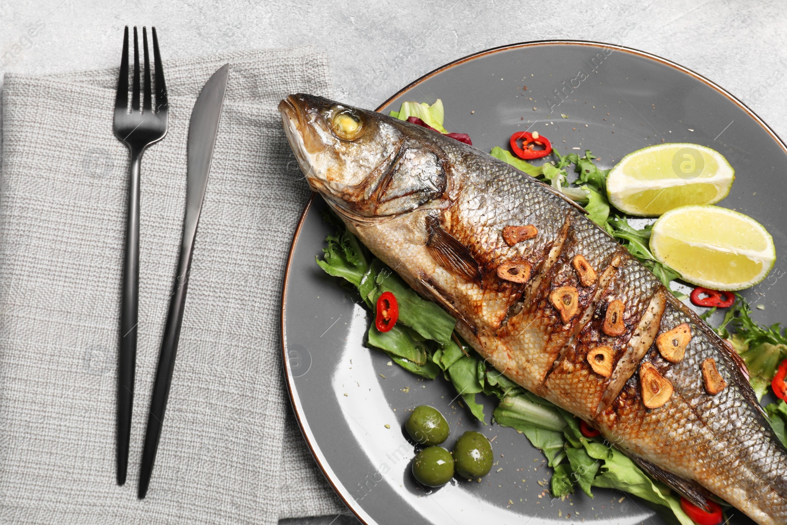 Photo of Delicious sea bass fish and ingredients served on light grey table, flat lay