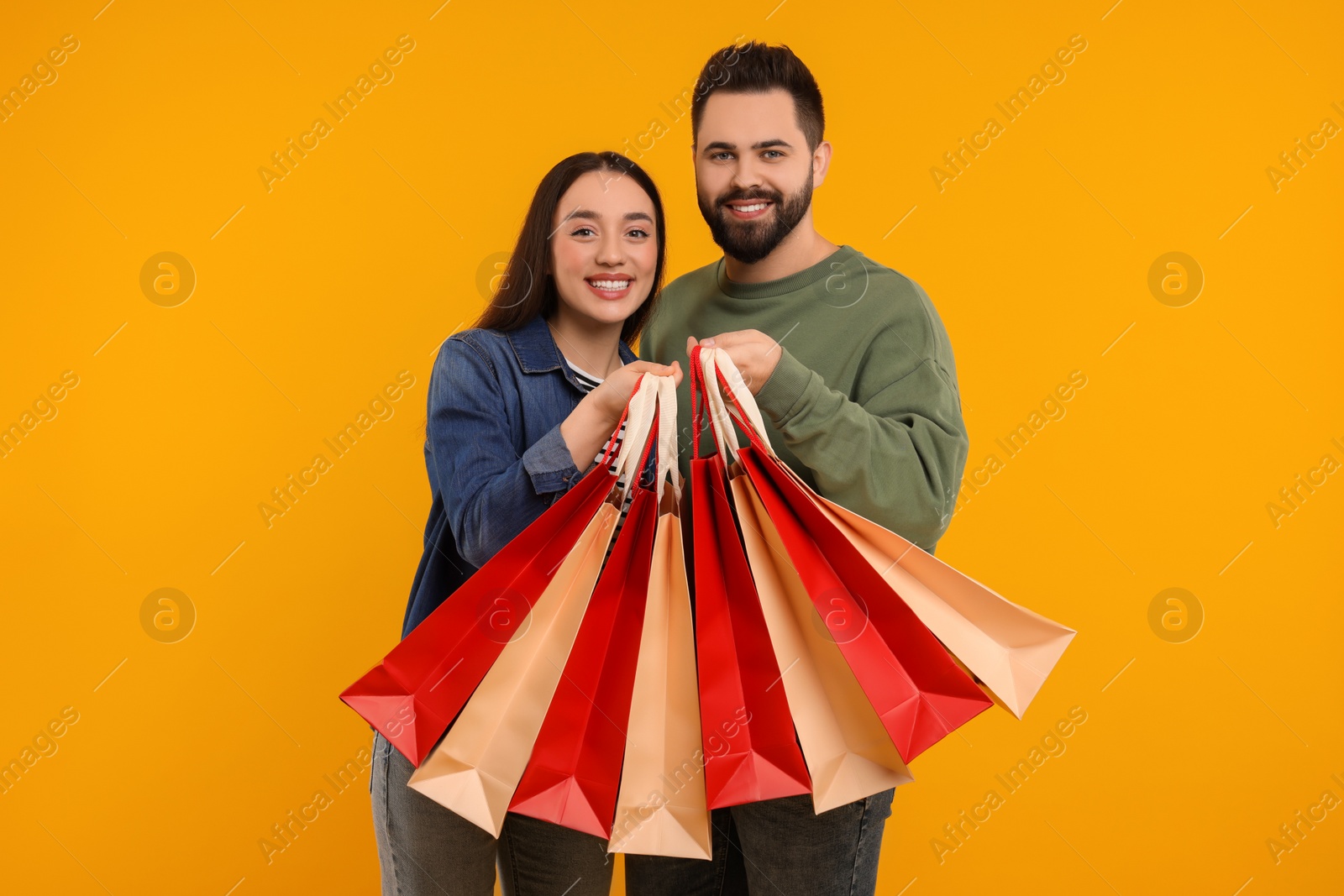 Photo of Happy couple with shopping bags on orange background