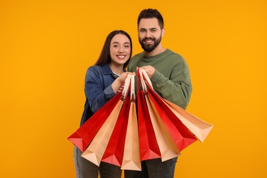 Happy couple with shopping bags on orange background