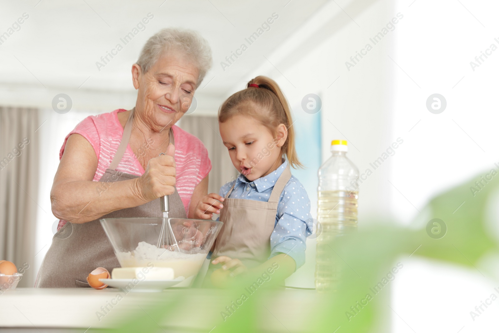 Photo of Cute girl and her grandmother cooking in kitchen