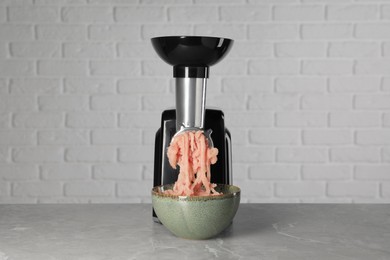 Photo of Electric meat grinder with chicken mince on grey marble table near white wall