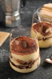 Photo of Delicious tiramisu in glasses on grey textured table, closeup