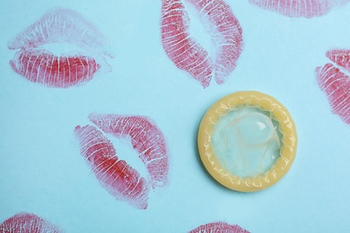 Condom with lipstick kiss marks on light blue background, top view. Safe sex