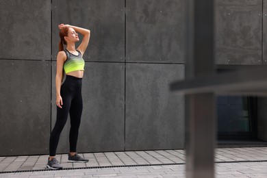 Photo of Beautiful woman in stylish gym clothes posing near grey wall on street