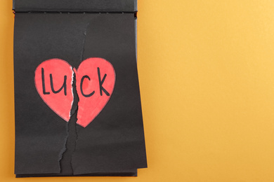 Torn heart and word LUCK written in notebook on orange background, top view. Space for text