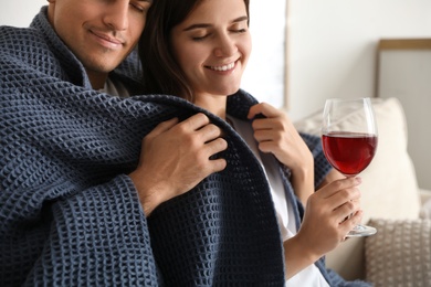 Happy couple covered with warm dark blue plaid at home, closeup