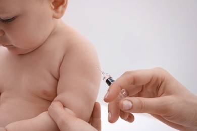 Doctor vaccinating baby against light background, closeup. Health care