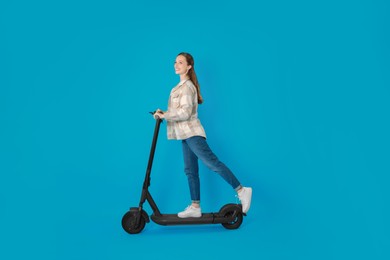 Happy woman riding modern electric kick scooter on light blue background