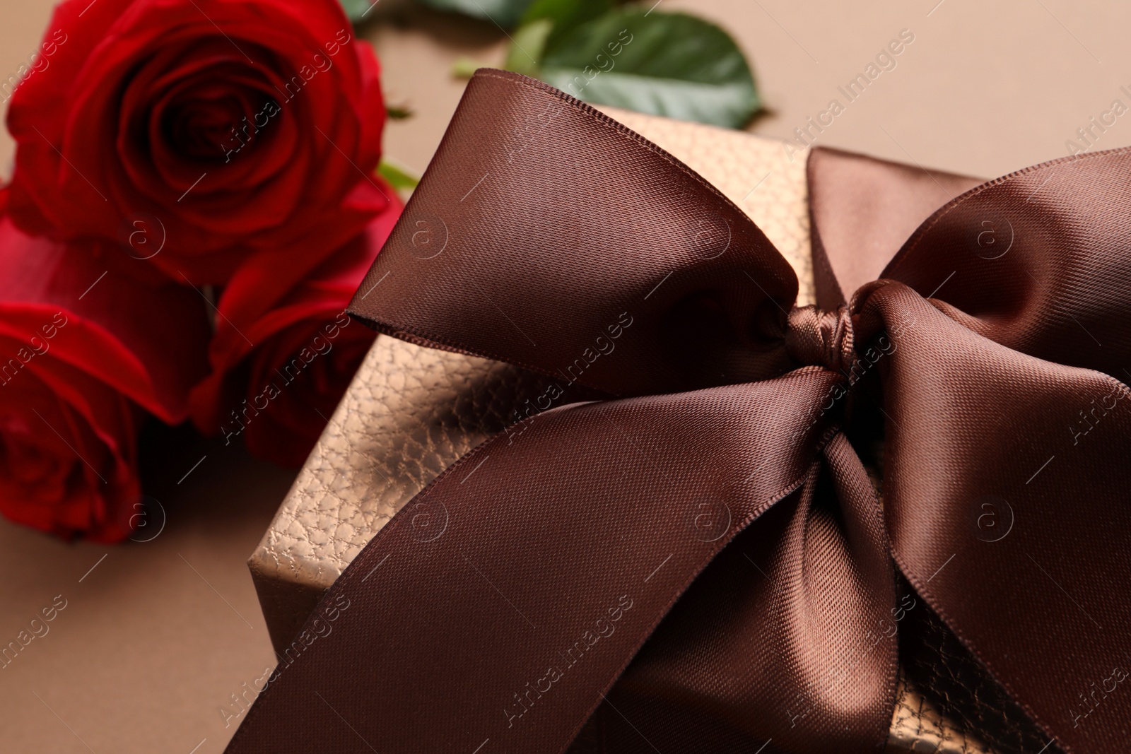 Photo of Beautiful gift box and flowers on brown background, closeup