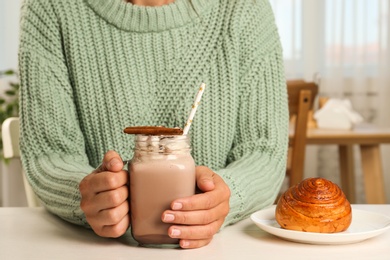 Woman holding mason jar of delicious cocoa drink with marshmallows at white table, closeup